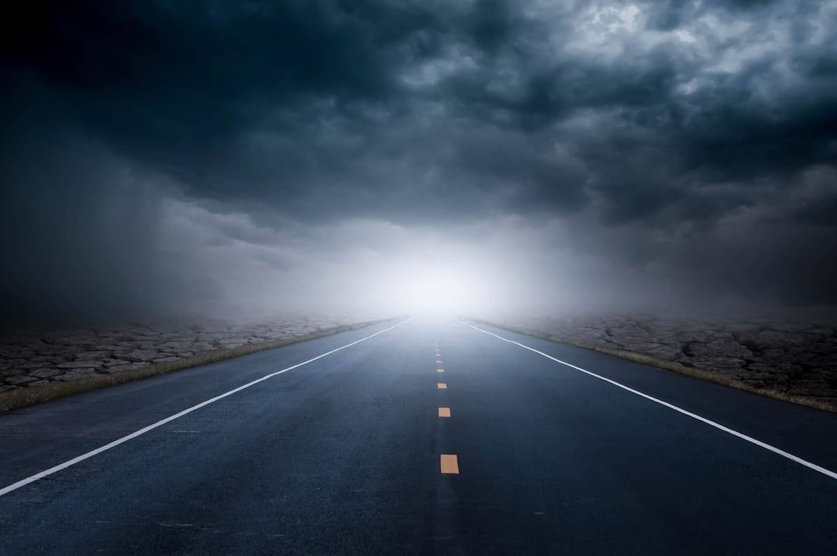 The road cuts through the cracked ground on a rainy day heading toward clear sky and light.