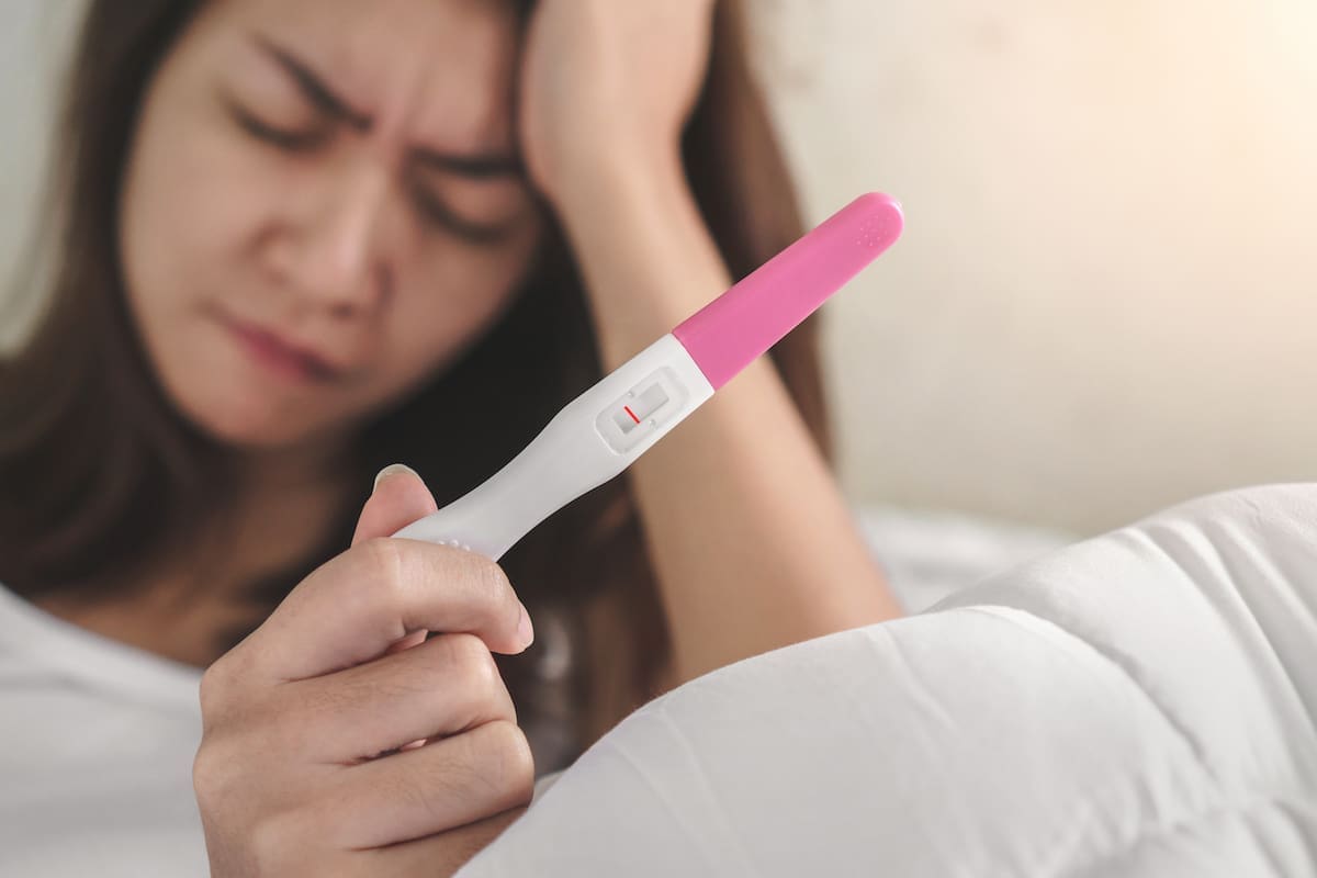 A woman who looks sad because she is childless holding a negative pregnancy test.