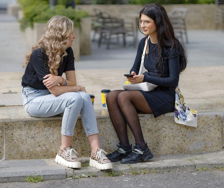 Two women sitting in public picnic area talking. 