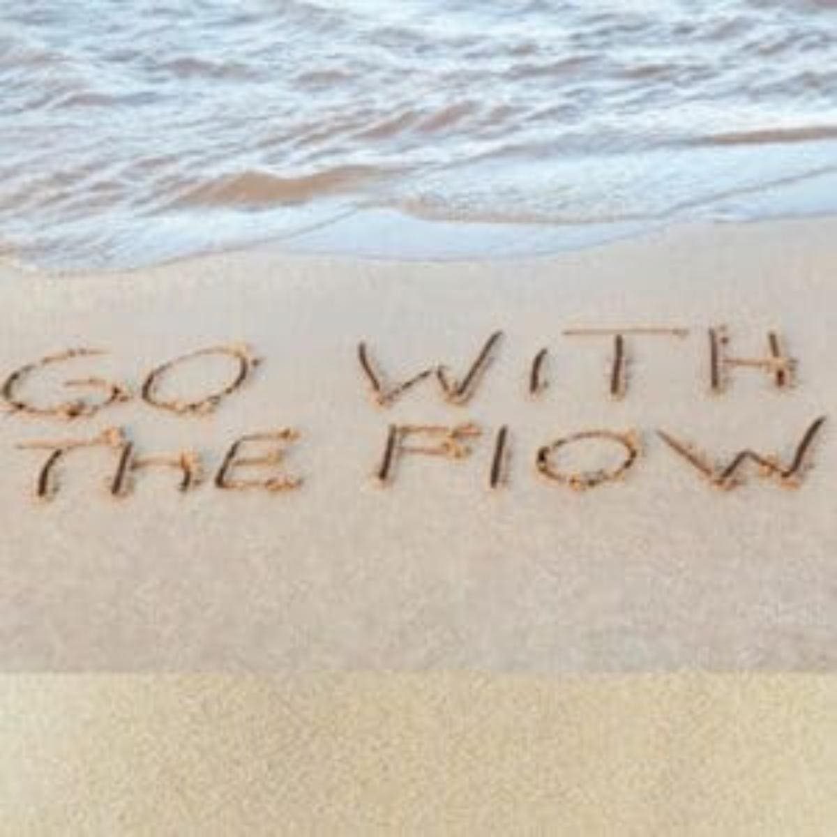 Ocean beach with "go with the flow" written in sand