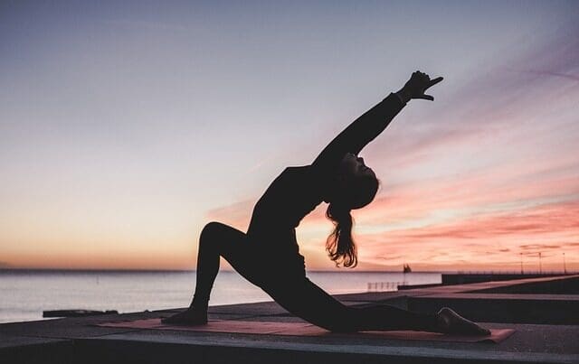 A woman does yoga outside near the water during a sunrise. To tie in what karma quotes have to do with Yoga.