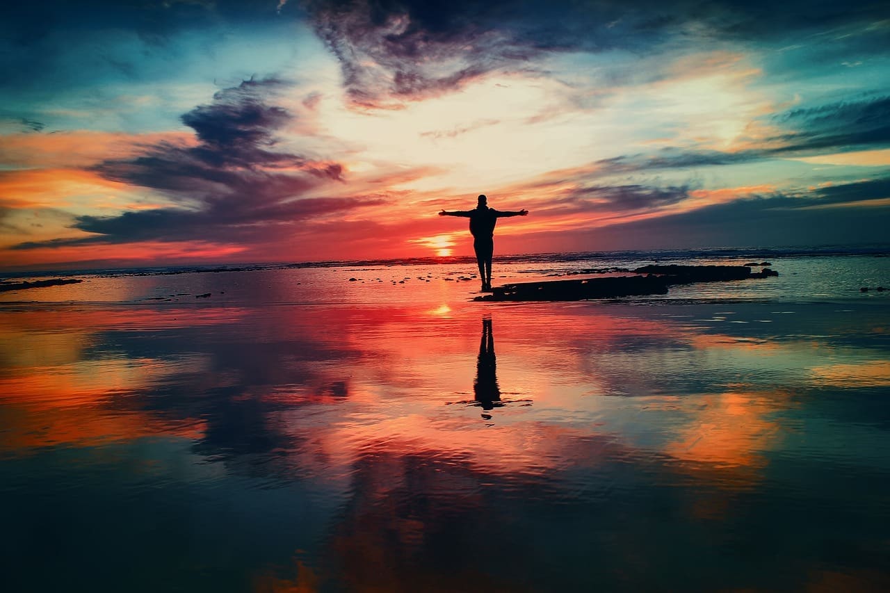 Silhouette of resilient person against the ocean with a rainbow-colored sunset