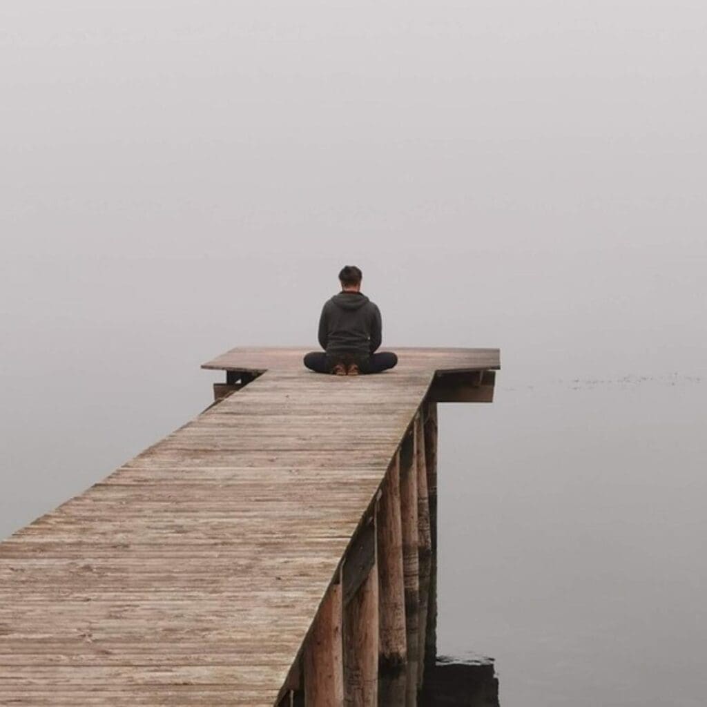 Man sitting on a dock meditating in front of serene foggy lake