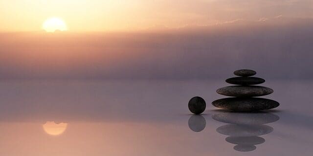 Stacked stones reflecting on the water in front of a serene sunset