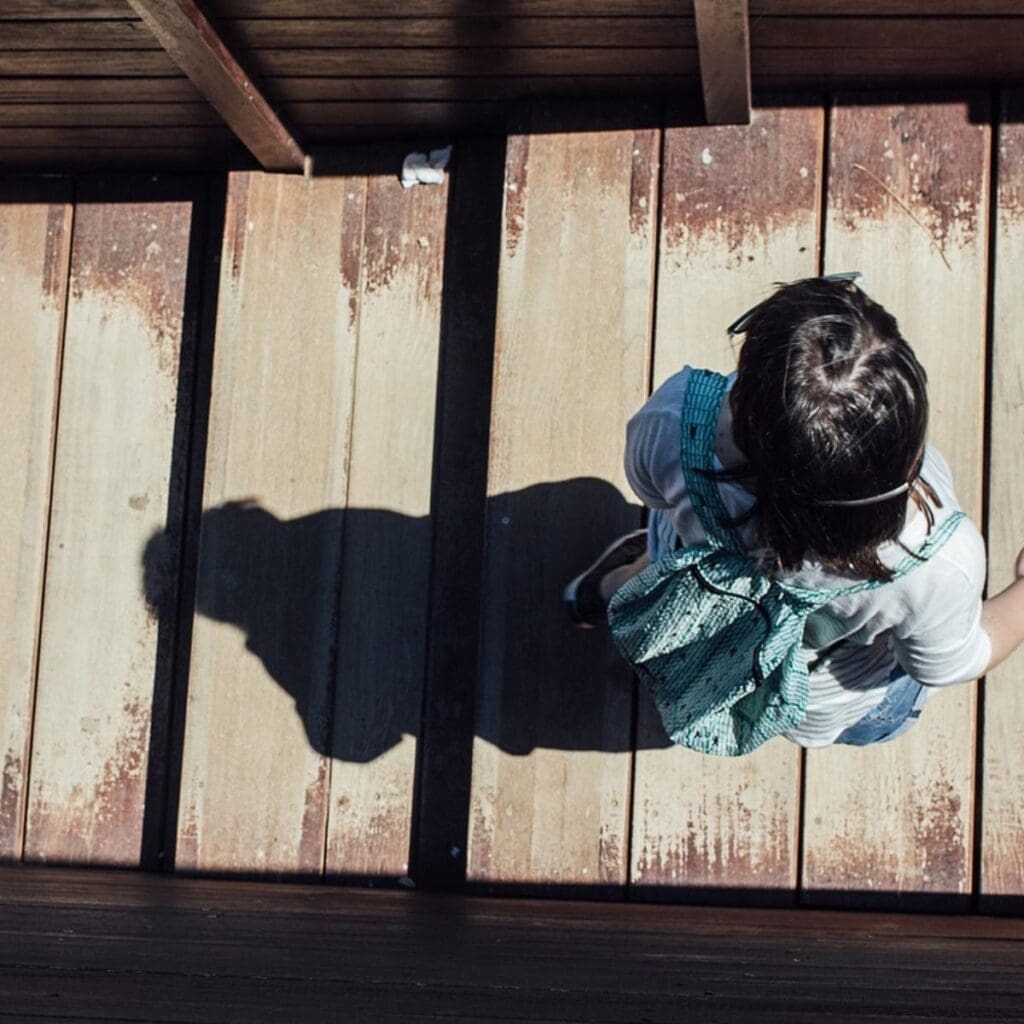 Aerial shot of girl walking along dock, shadow cast behind her. 