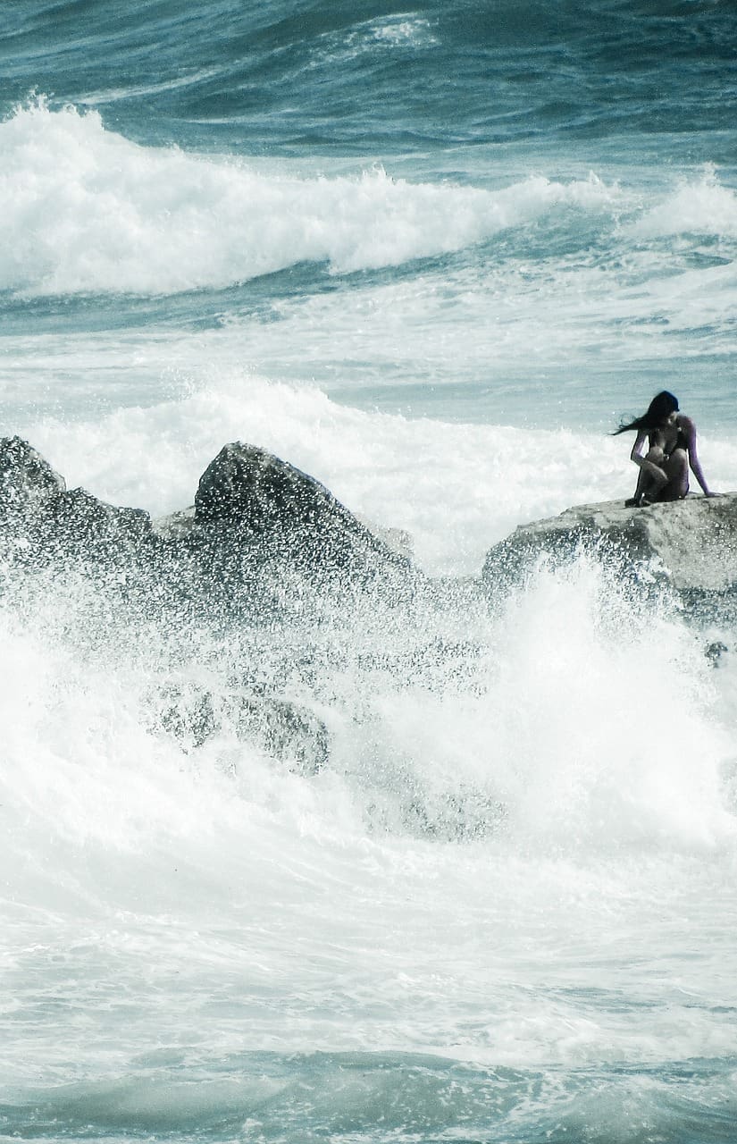 Woman sitting in solitude on rock amongst giant crashing ocean waves