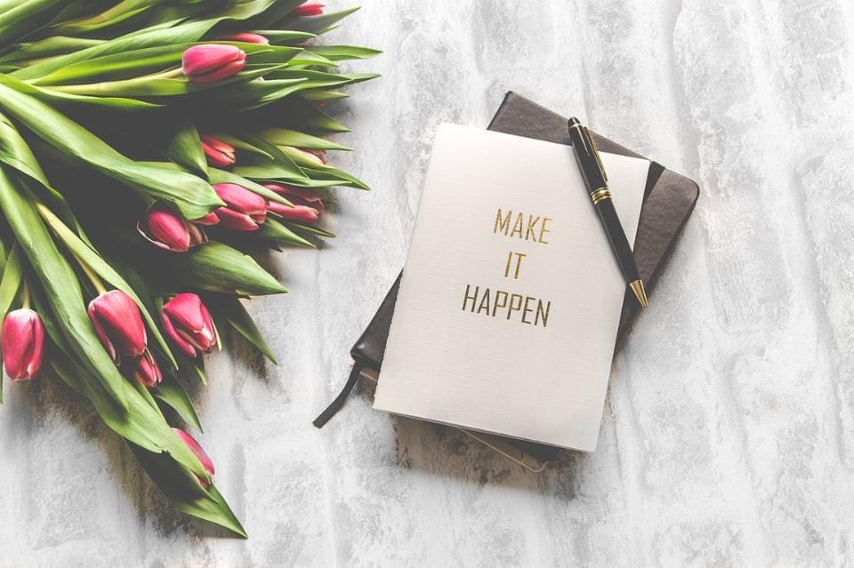 Bouquet of red tulips next to a day planner with a note that says "Make it Happen" and a pen sitting on top of it. 