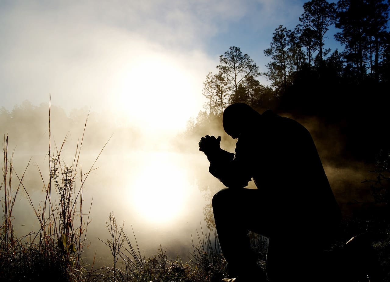 Man's silhouette illuminated by rising sun sitting near foggy lake