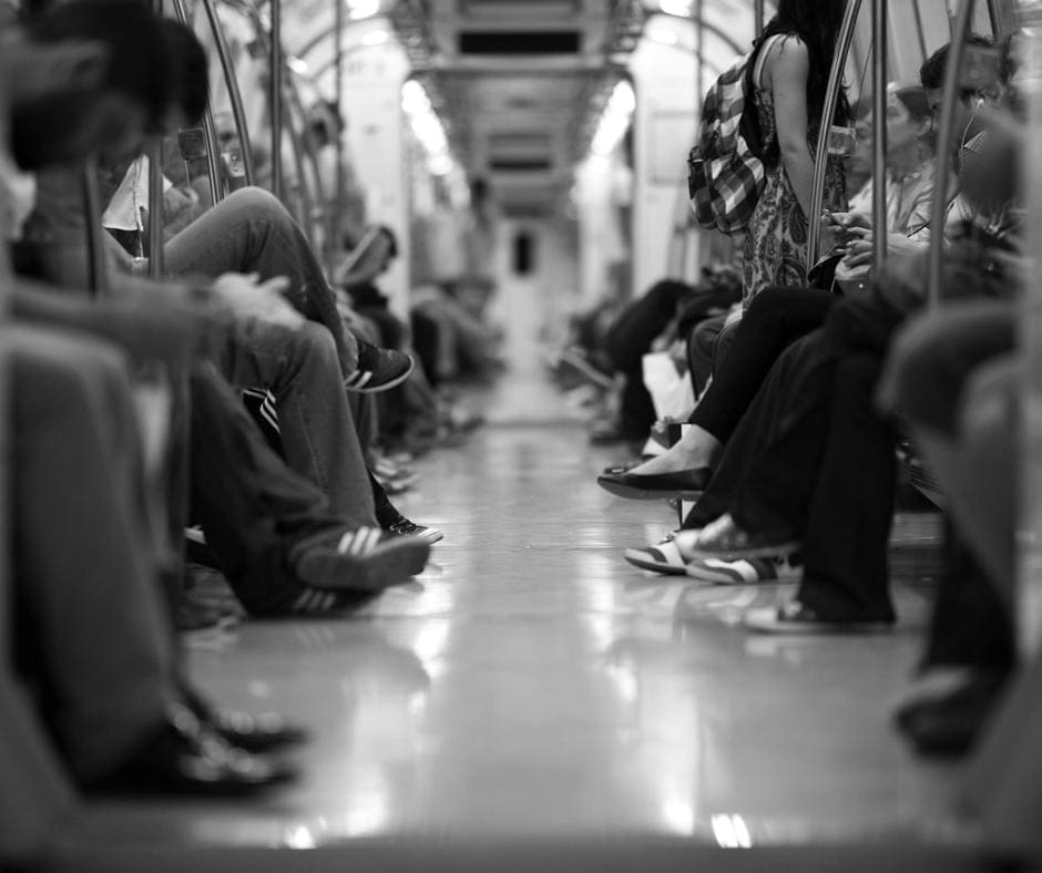 Black and white photograph of a subway train car aisle, showing all different kinds of feet in shoes. 