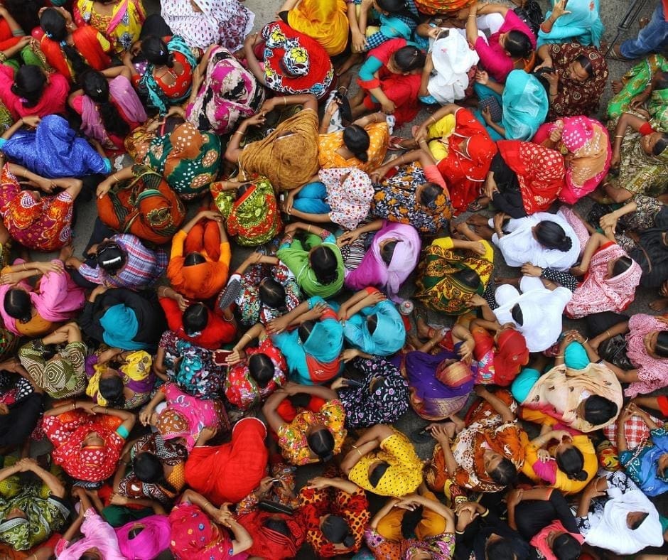 Photo of a crowd of women all sitting together, each one dressed in brightly colored garments depicting authenticity and be true to yourself. 