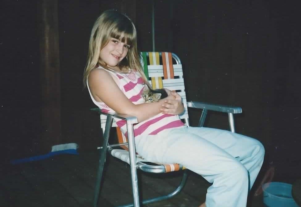 Young Donna sitting on the porch in the evening, snuggling a calico kitten.