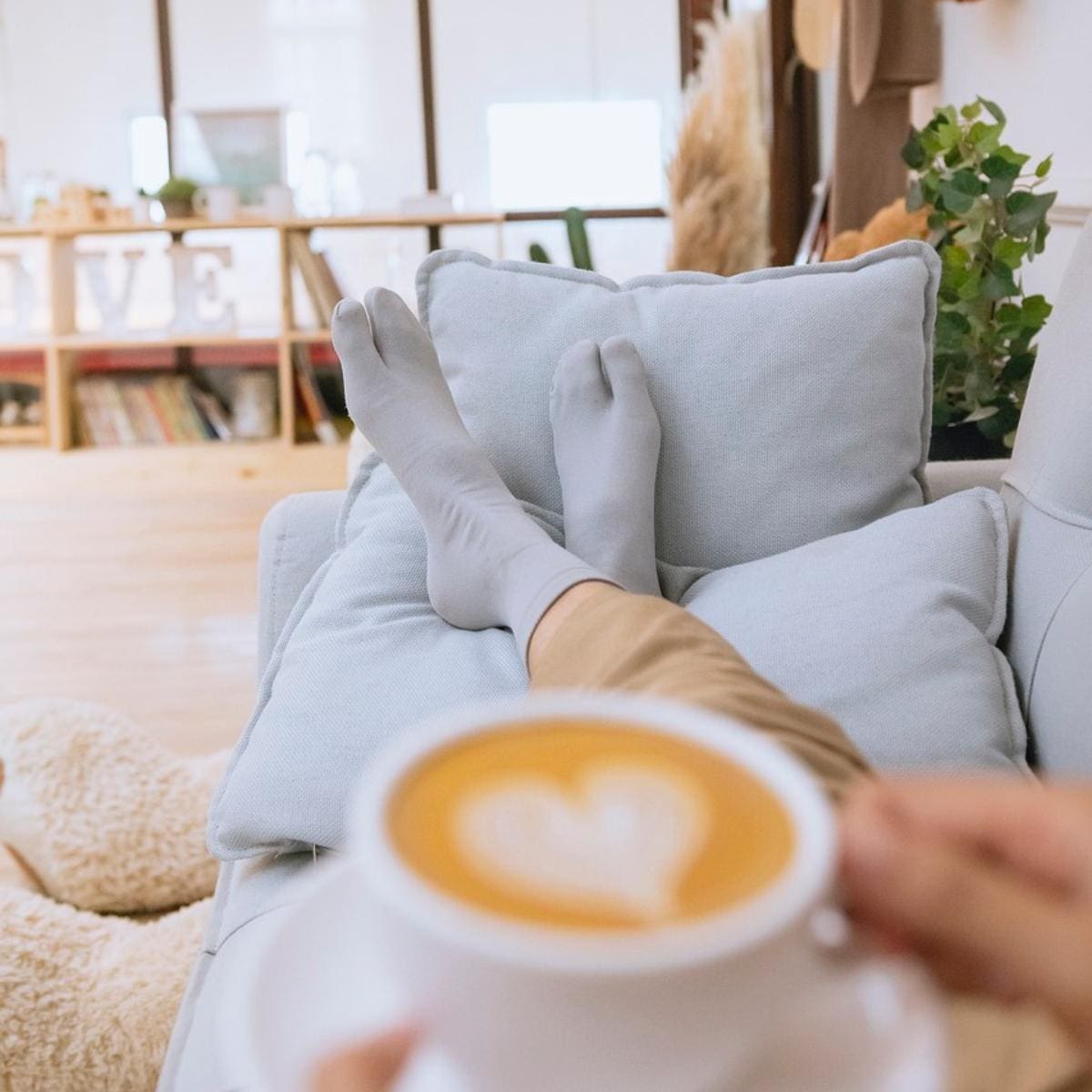 Person relaxing on couch with socks on drinking cappuccino with heart foam art