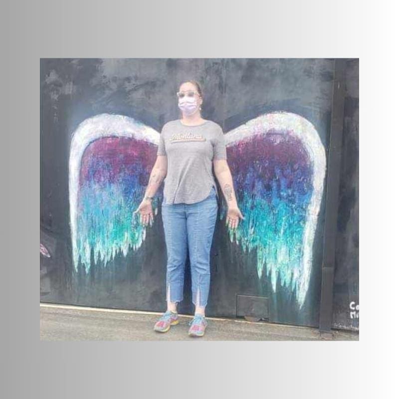 A photo of the author standing in front of angel wings. A reminder to her that she is here and a suicide survivor.