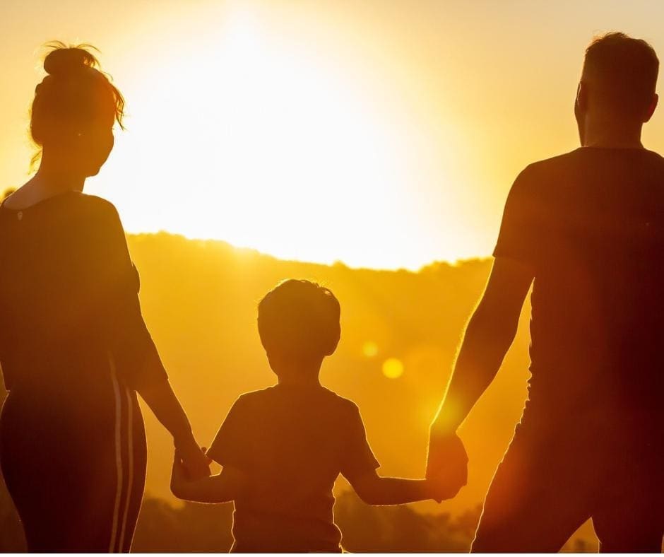 Family (man, woman, child) holding hands and watching the sunset 