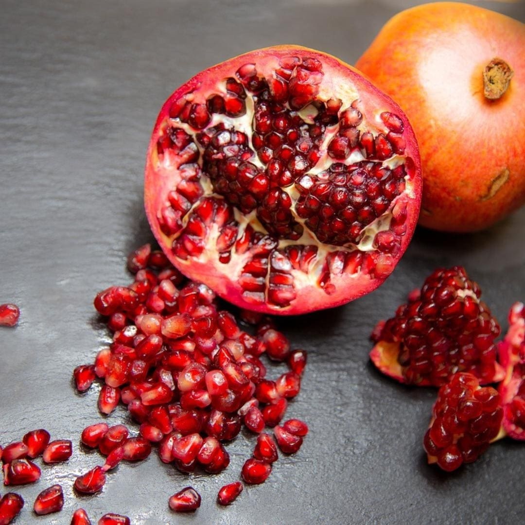 Photo of a cross-section of a pomegranate with seeds spilled out. 