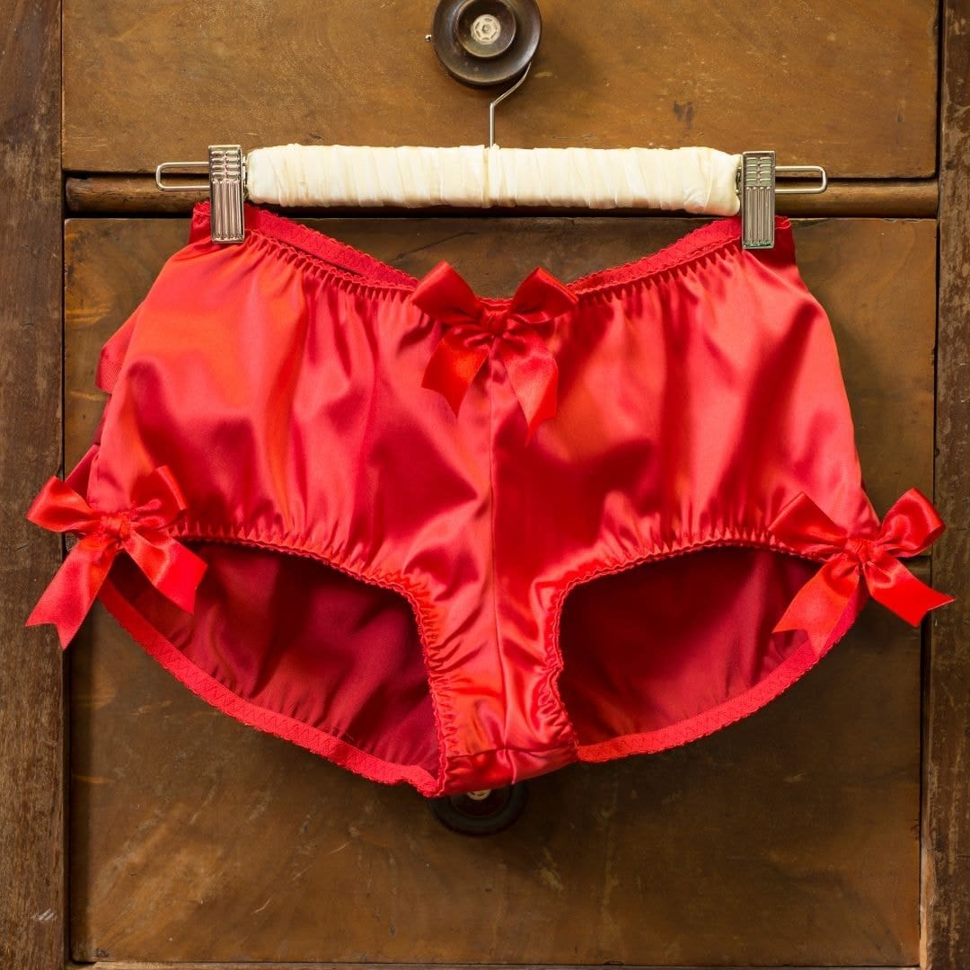 Photo of red underwear hanging on a hanger on a brown dresser drawer. 